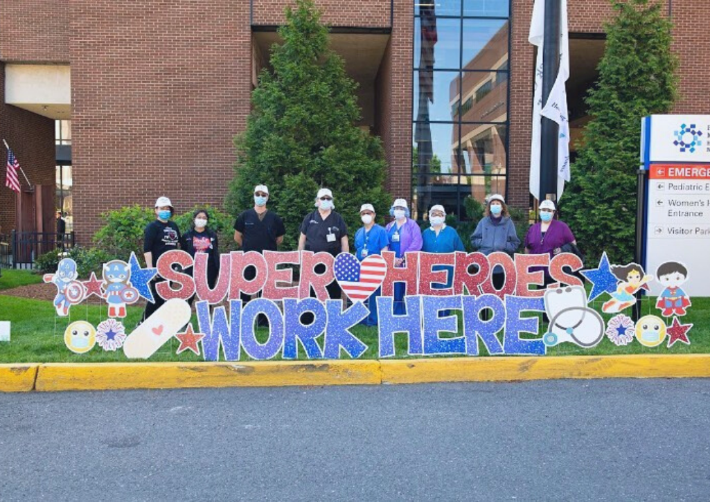 People standing next to a sign that says Super Heroes Work Here. They are outside a hospital