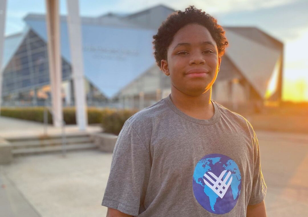 A Black boy wearing a GivingTuesday tshirt with the sun setting behind him