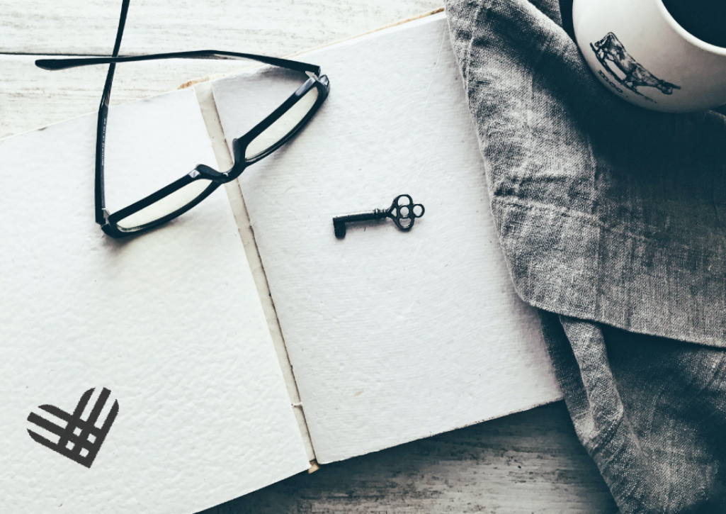 A sketchbook opened with a GivingTuesday logo drawn on it. Eyeglasses and a key are on top and a coffee mug to the left. The image is in black and white