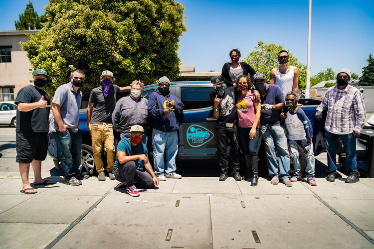 A large group of people standing in front of a dark blue car.