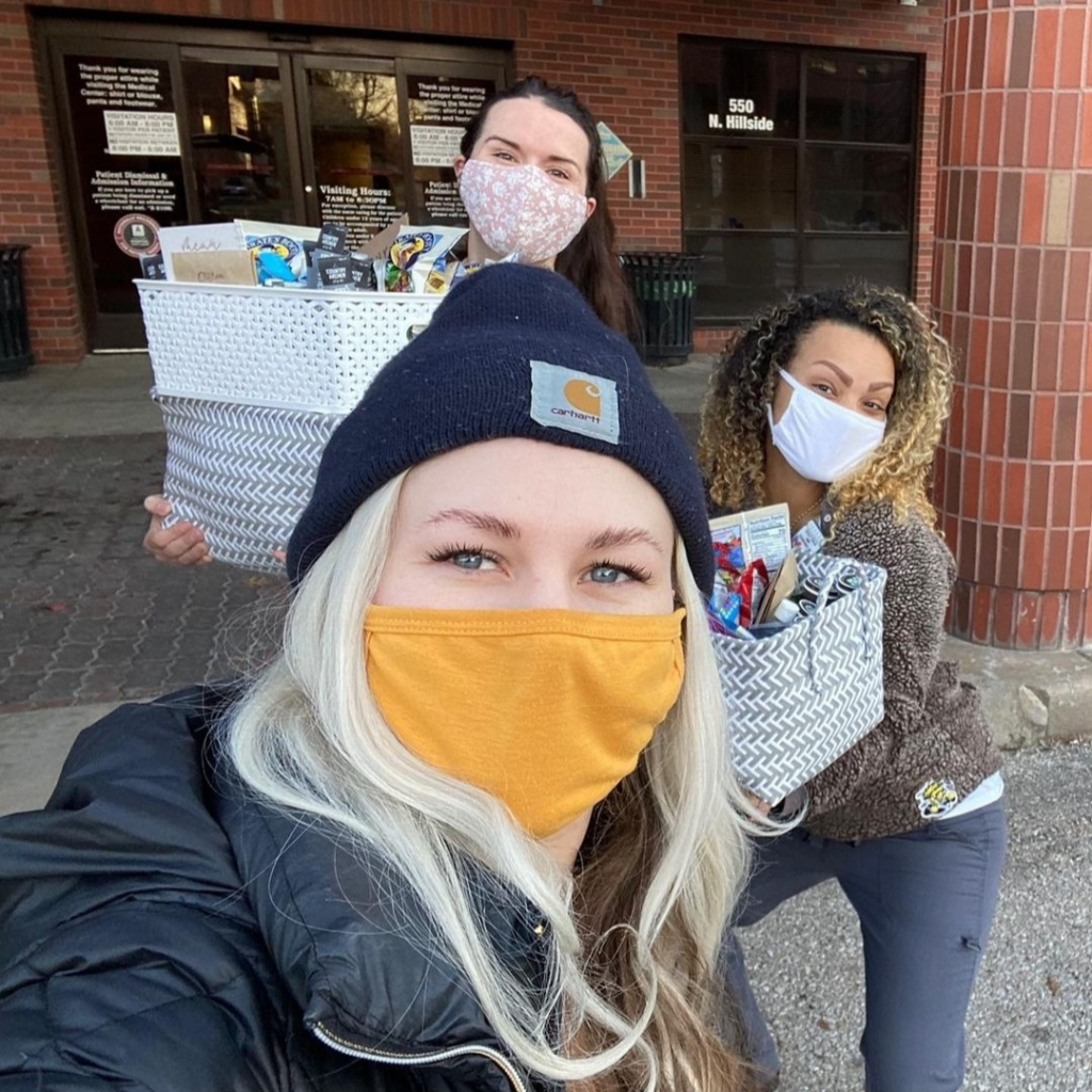 Women wearing masks holding gift baskets that they're about to give to nurses at a hospital