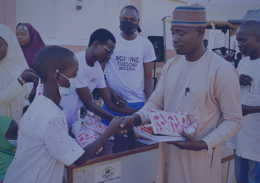 A man wearing a GivingTuesday tshirt handing a mask to a child.