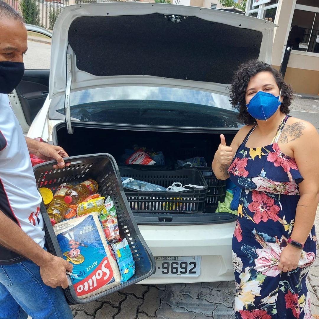 Two Brazilians stuffing a car trunk with food. One is giving a thumbs up. 