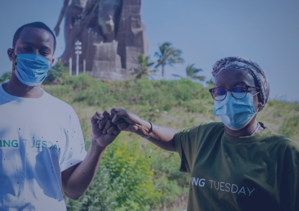 An African man and an African woman fist bumping. Both are wearing masks and GivingTuesday tshirts