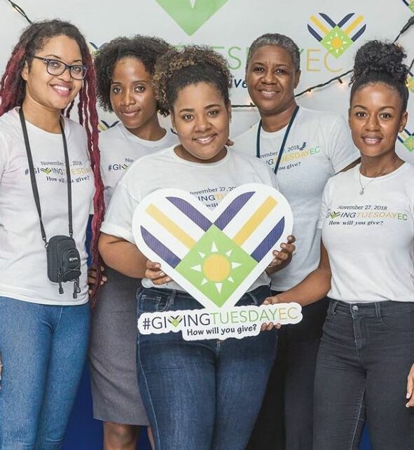 Eastern Caribbean GivingTuesday team standing by a step and repeat in pre-pandmic times, holding a GT heart logo