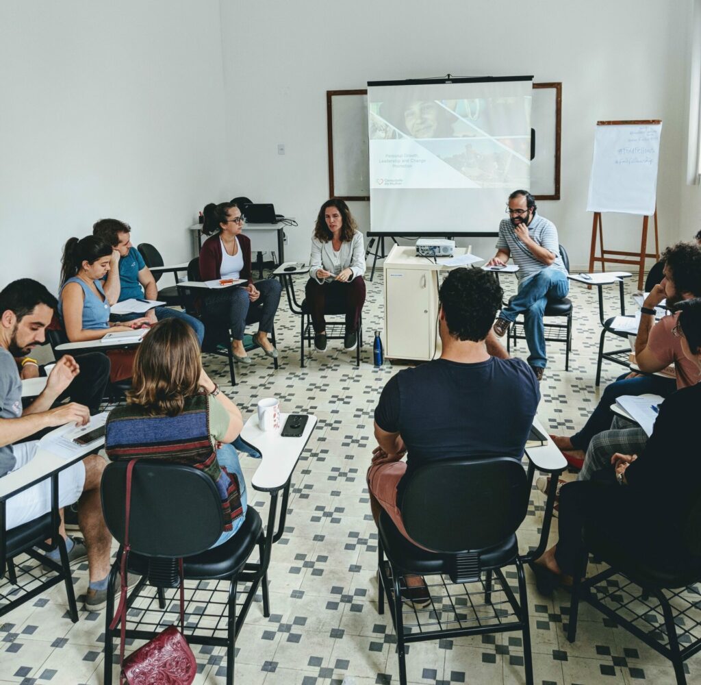A group of people sitting in chairs in a circle (pre-pandemic), listening to a lecture and getting ready to brainstorm