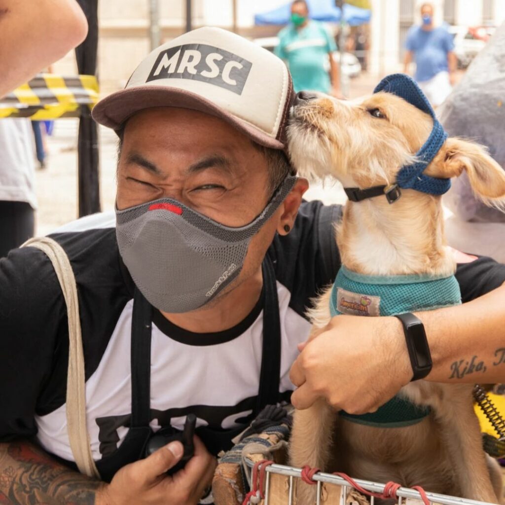 a smiling man wearing a mask getting a kiss from a dog