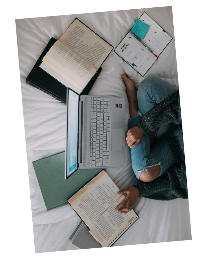 A student sitting on a bed with a laptop and books around them